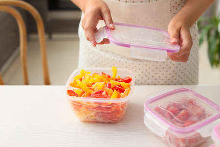 Woman holding plastic container with frozen vegetables in kitchen