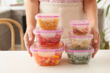 Woman holding plastic containers with frozen vegetables in kitchenの写真素材