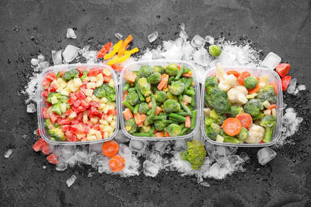 Plastic containers with frozen vegetables and ice on dark backgroundの写真素材