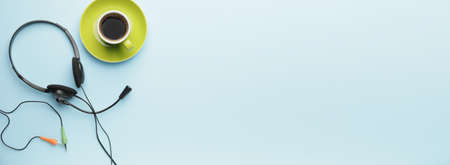 Headset with cup of coffee on color background with space for text