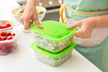 Woman holding plastic containers with frozen vegetables in kitchenの写真素材