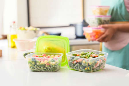 Woman holding plastic containers with frozen vegetables in kitchen