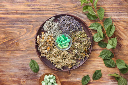 Plate with dry herbs and plant based pills on wooden backgroundの写真素材