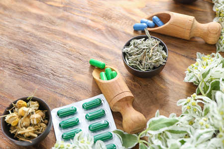 Plant based pills and dry herbs on wooden background