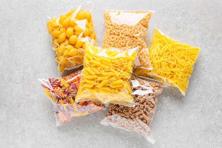 Bags with different uncooked pasta on light background