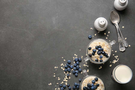 Bowls with tasty oatmeal and blueberry on dark table