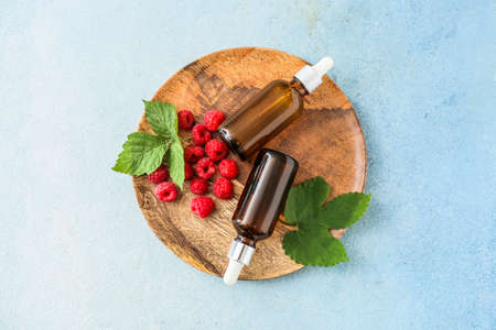 Bottles of raspberry essential oil on color background