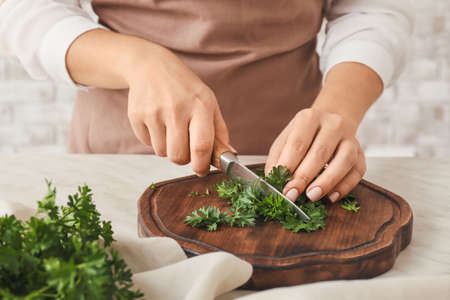 Woman cutting fresh parsley at table, closeup