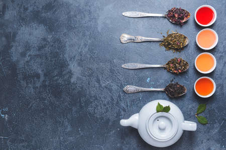 Teapot, cups and spoons with different dry tea leaves on dark backgroundの写真素材