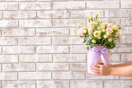 Hands with bouquet of beautiful flowers on brick backgroundの写真素材