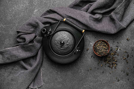 Composition with teapot and dry tea leaves on dark background