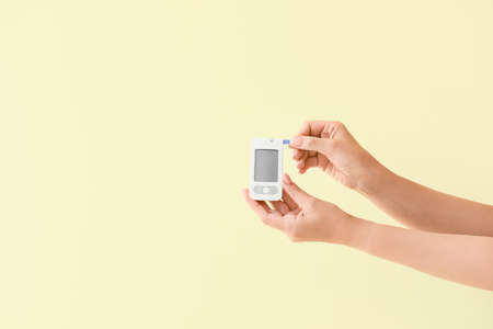 Female hands with glucometer on color background. Diabetes concept