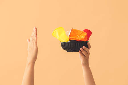 Female hands with plastic tableware on color background. Ecology concept