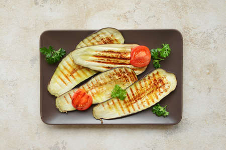 Tasty grilled eggplant with tomato and parsley in plate on light background