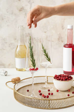 Woman making cocktail with champagne, cranberry and rosemary on light table