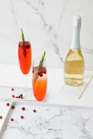 Glass of champagne cocktail with cranberry and rosemary on light table