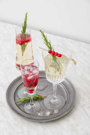 Glass of champagne cocktail with cranberry and rosemary on light table