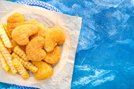 Tasty nuggets and french fries in plate on color background