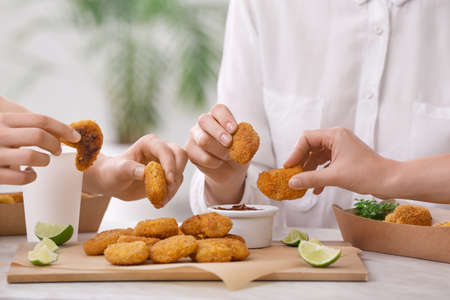 Women eating tasty nuggets with ketchup on table in room