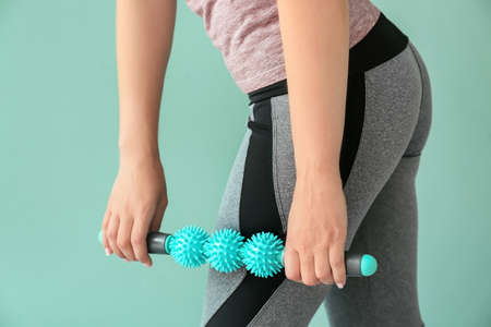 Sportswoman massaging herself with body roller on color backgroundの写真素材