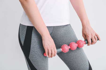 Sportswoman massaging herself with body roller on light background