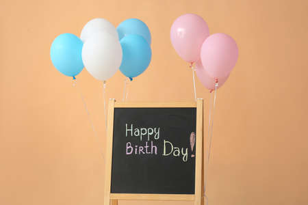 Chalkboard with written text HAPPY BIRTHDAY and air balloons on color backgroundの写真素材