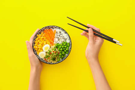 Woman eating tasty rice poke bowl on color backgroundの写真素材