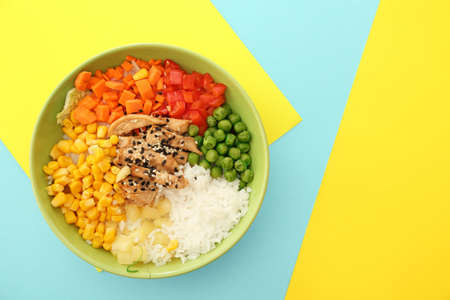 Bowl with tasty rice, chicken and vegetables on color backgroundの写真素材