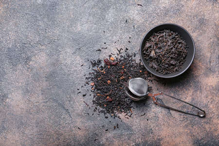 Dry black tea leaves in bowl and infuser on grunge backgroundの写真素材