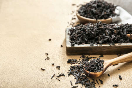 Dry black tea leaves in spoon and bowl on color background
