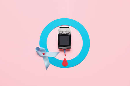 Glucometer with blue ring and awareness ribbon on color background. Diabetes concept