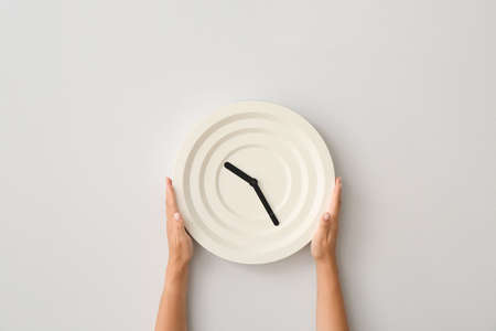 Female hands with clock on light wallの写真素材