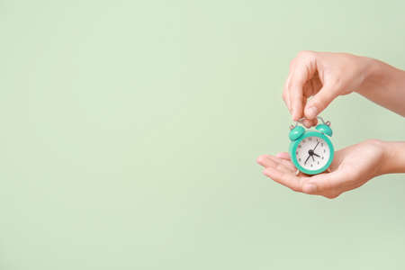Female hands with alarm clock on color backgroundの写真素材