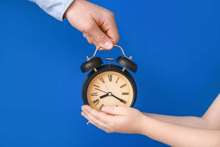 Hands of family with alarm clock on color backgroundの写真素材