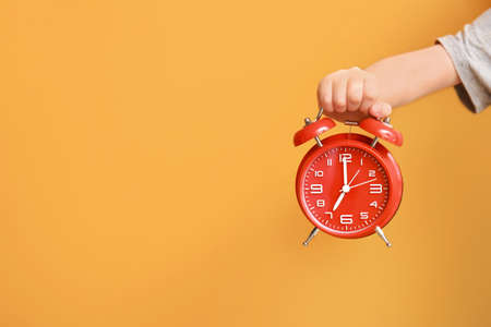 Child's hand with alarm clock on color background