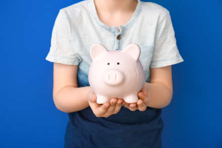 Child holding piggy bank on color backgroundの写真素材