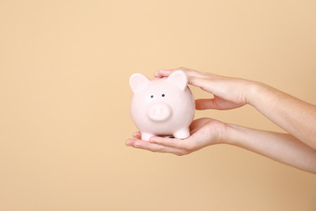 Female hands with piggy bank on color backgroundの写真素材