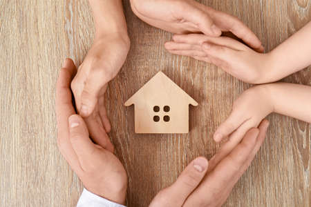 Hands of family with figure of house on wooden backgroundの写真素材