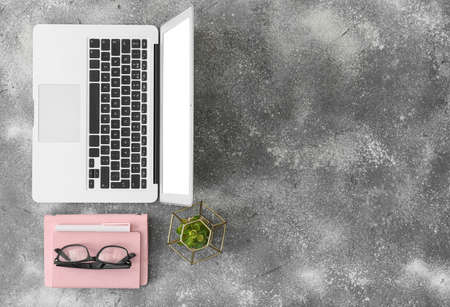 Modern laptop with stationery and eyeglasses on gray background
