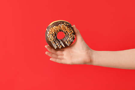 Hand with tasty donut on color backgroundの写真素材
