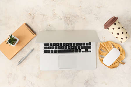 Modern laptop with stationery and cup of coffee on light backgroundの写真素材