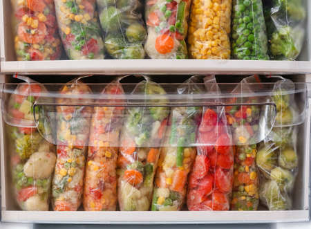 Plastic bags with frozen vegetables in refrigerator, closeup