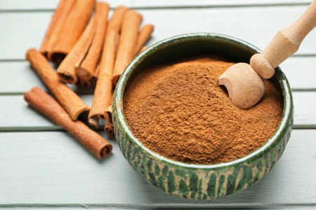 Bowl with cinnamon powder and sticks on wooden backgroundの写真素材