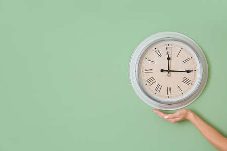 Female hand with clock on color wallの写真素材