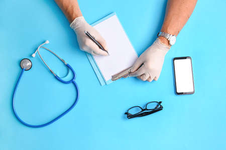 Male hands in medical gloves with blank paper sheet and stethoscope on color backgroundの写真素材