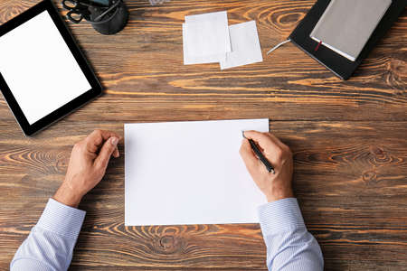Male hands with blank paper sheet and tablet computer on wooden backgroundの写真素材