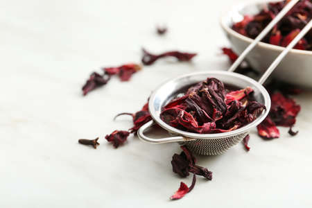 Sieve with dry hibiscus tea on white background
