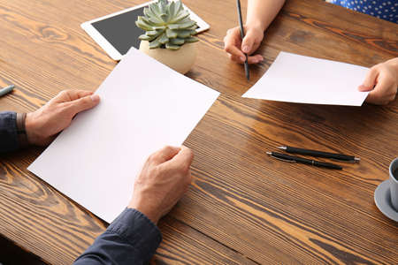 Hands with blank paper sheets on wooden background