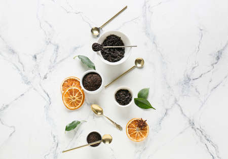 Bowls with dry black tea leaves, dried fruits and spoons on light backgroundの写真素材