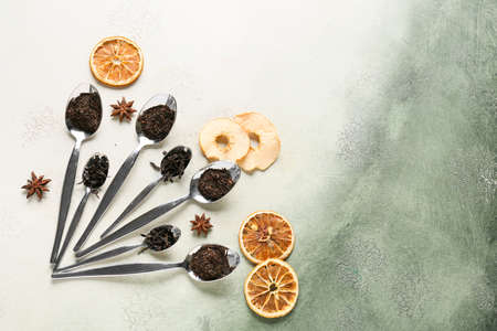 Spoons with dry black tea leaves and dried fruits on light background